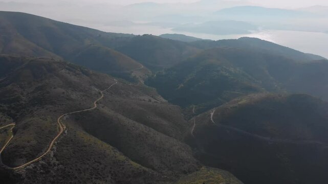 An expansive aerial view showcases a winding road traversing the verdant, mountainous landscape of Corfu Island, Greece.
