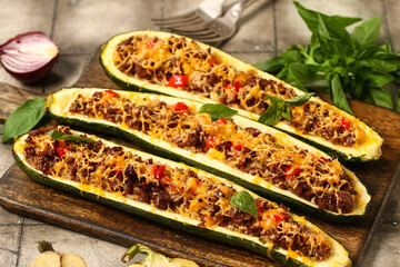 Wooden board with meat stuffed zucchini boats on grey tile background