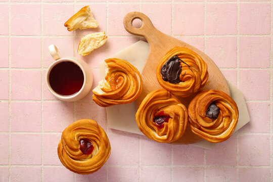 Wooden board with tasty cruffins and cup of tea on pink tile background