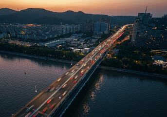 Cars traverse the illuminated blue bridge spanning the river at night with vibrant city skyline in view. Hangzhou, China.