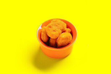 Bowl with tasty nuggets on yellow background