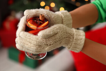 Young woman with glass of mulled wine at home on Christmas eve, closeup