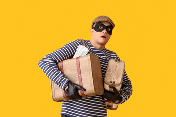 Male thief with briefcases of money on yellow background