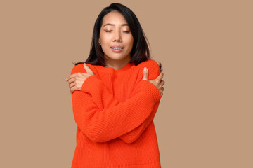 Young Asian woman hugging herself on brown background