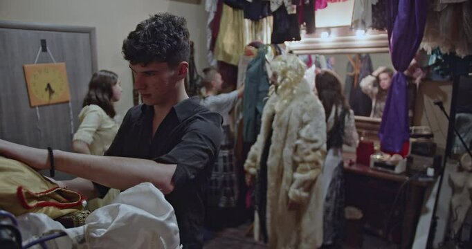 Actors prepare backstage before a theatre play. They dress up in various costumes and chat, waiting for their turn to perform.
