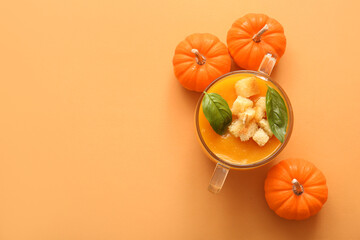 Glass pot of delicious pumpkin cream soup with croutons and basil on orange background