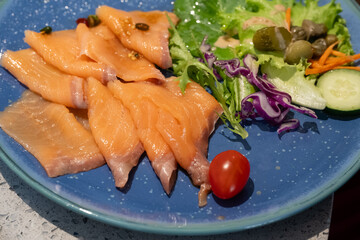 A beautifully plated dish of smoked salmon slices served with a colorful fresh salad on a blue ceramic plate.