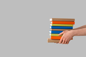 Hands holding stack of books on grey background