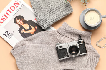 Stylish warm clothes with photo camera and cup of coffee on beige background