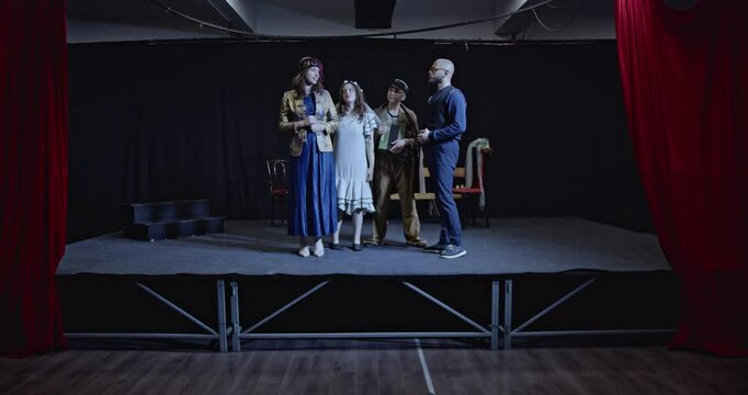 Young actors rehearse a play on stage with their director. They practice their lines and movements under his guidance.