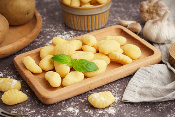 Wooden board with tasty gnocchi and basil on grunge background, closeup