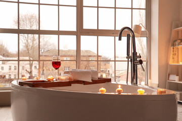 Bathtub with wine and burning candles in room