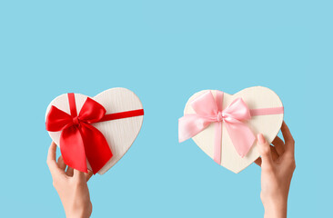 Female hands with gift boxes in shape of heart on blue background. Valentine's Day celebration