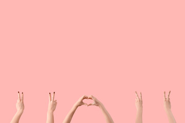 Female hands showing peace and heart gestures on pink background