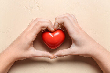 Fototapeta premium Female hands with red heart on beige background