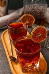 Wooden tray with glasses of Old Fashioned Cocktail, dried orange slices and spoon on grey grunge background