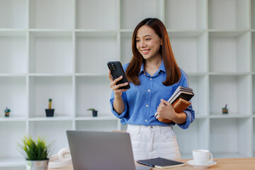 Portrait of smiling smart teenage girl holding phone looking at camera standing in modern classroom, copy space. Back to school, education concept