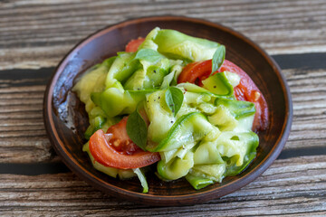 Vegetable salad with raw pickled zucchini and fresh tomatoes on clay plate on wooden table, side view, close up. Healthy eating
