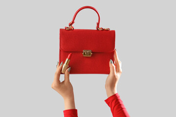 Female hands with stylish women's bag and lipstick on grey background