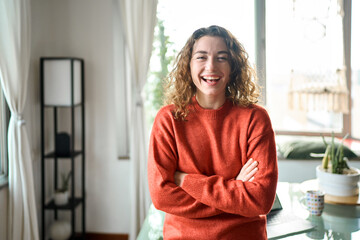 Happy beautiful positive woman wearing orange sweater standing in modern cozy apartment living room...