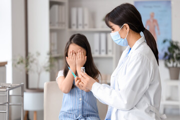 Female doctor with syringe and ampule vaccinating scared little girl in clinic