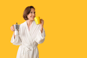 Beautiful young happy woman in bathrobe with cezve and cup of coffee on yellow background