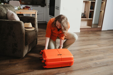 Woman packs orange suitcase at home in preparation for summer vacation trip filled with excitement...