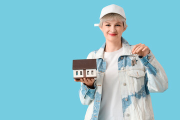 Portrait of beautiful young woman with house model and keys on blue background. Mortgage concept