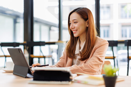 Young busy professional asian business woman company executive or entrepreneur using digital tablet working sitting at desk in office looking at tab, managing financial project data.