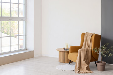 Cozy armchair with plaid near coffee table and plant in living room
