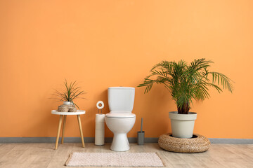 Interior of restroom with toilet bowl, coffee table and plants near beige wall