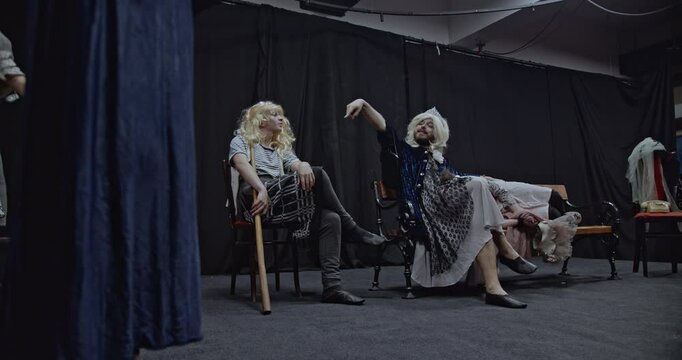 Actors in costume rehearsing a play on a theater stage. They are discussing their roles and practicing their lines.