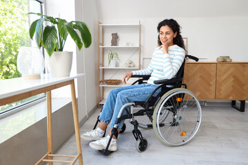 Young African-American woman in wheelchair near window at home