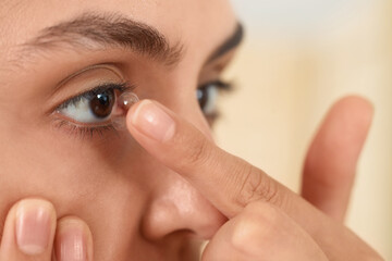 Young woman putting in contact lenses at home, closeup