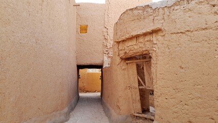 A photo of the old mud houses in Najd, Saudi Arabia, featuring wooden doors, earthen walls, narrow...
