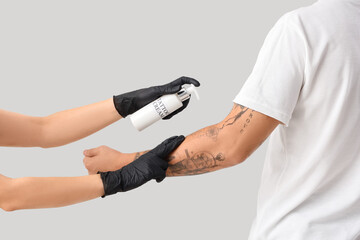 Tattoo master applying cream on man's arm against light background, back view