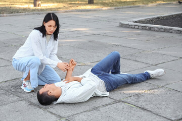 Young woman checking pulse of her husband having heart attack on street