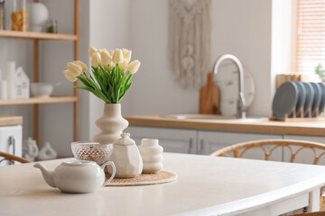 White dining table with teapot and vase of flowers in interior of kitchen