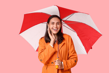 Happy young woman with umbrella on pink background