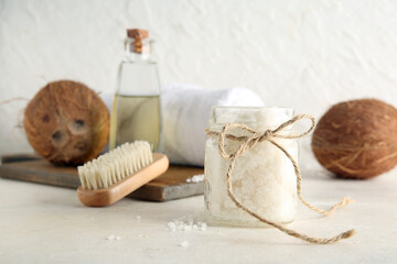 Jar of natural body scrub, massage brush, towel and coconuts on light background