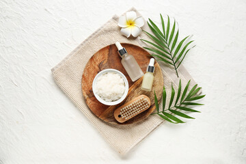 Composition with natural body scrub, essential oil, massage brush and palm leaves on light background