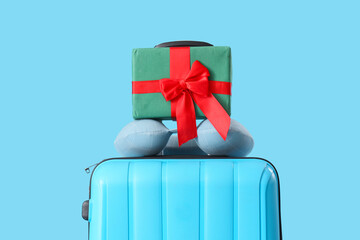 Suitcase with Christmas gift boxes and neck pillow on blue background. Closeup