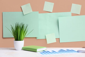 Blank papers and grass with diagram on table near beige wall. Green Energy concept