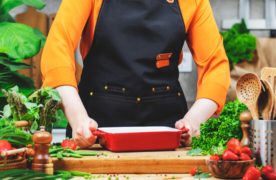 passionate woman chef holds a ceramic baking dish prepares a healthy meal in a cozy kitchen filled with fresh vegetables and farm herbs.
