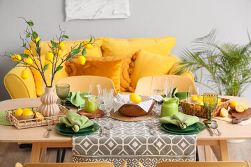 Stylish green table setting decorated with many fresh citruses and beautiful lemon tree branches in dining room