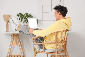 Young man working with laptop near table at home, back view