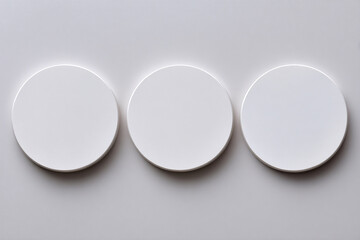 Three blank white round coasters or disks evenly spaced on light gray background