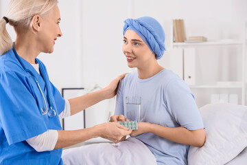 Young woman after chemotherapy taking pills from nurse in hospital room. Brain cancer concept