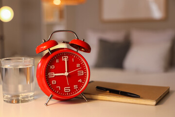 Alarm clock, glass of water and notebook on table in room at evening, closeup