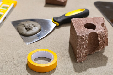 Trowel with cement, brick and construction tools on grey grunge background, closeup